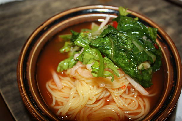 A person using chopsticks to pull delicious kimchi noodles from a hot pot. The bowl is filled with spicy kimchi, noodles, and fresh spring onions in a savory broth, creating a perfect meal for any occasion.