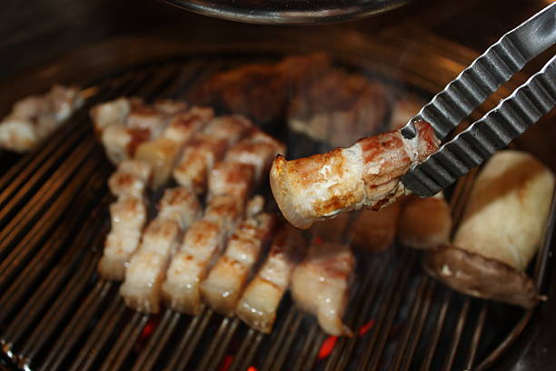A close-up of intense yellow flames dancing on a BBQ grill, creating a captivating visual effect. The reflective metal surface enhances the fiery glow, evoking a sense of heat and energy. The image captures the essence of outdoor grilling and barbecue preparation, making it perfect for themes of culinary arts, summer gatherings, and food events. The fiery movement and vibrant colors add a dramatic and artistic flair.