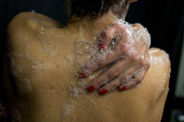 A woman reaching her back to apply cleansing foam. Focus on healthy skin, hydration, and the intimacy of daily beauty rituals.