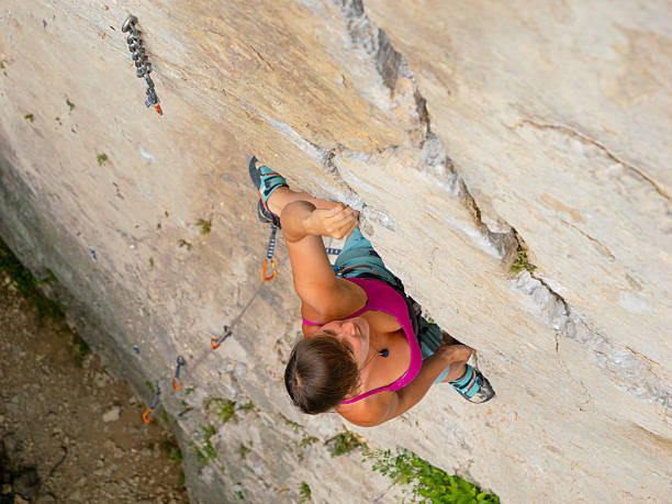 TOP DOWN, CLOSE UP: Sports climber in pink top climbs a limestone wall along a crack. Her posture and focus capture intensity and precise technique required when climbing in natural climbing area.