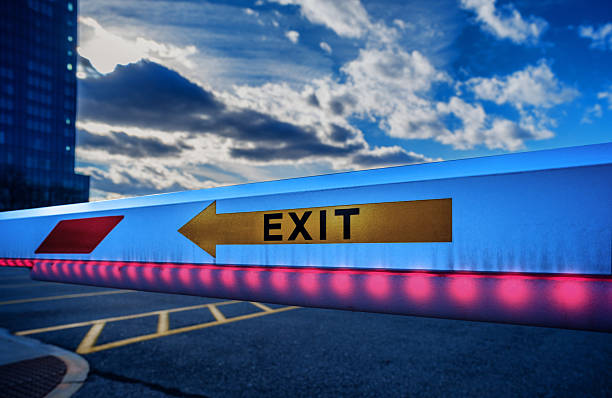 Boston, Massachusetts, USA - December 21, 2025: Close-up of a closed parking lot barrier gate with red LED lights and Exit sign at the twilight time of day.