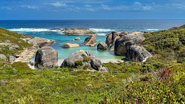 A serene coastal landscape features large boulders, turquoise ocean waters, and lush vegetation, evoking tranquility and natural beauty.
