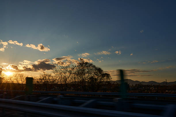 The sinking sun casts streaks of light through clouds, gently enveloping cars on the highway. A moment where the day's end meets the excitement of returning to a place of rest.