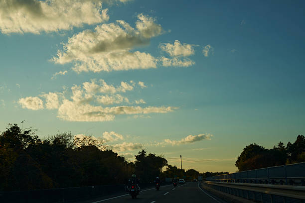 The sinking sun casts streaks of light through clouds, gently enveloping cars on the highway. A moment where the day's end meets the excitement of returning to a place of rest.
