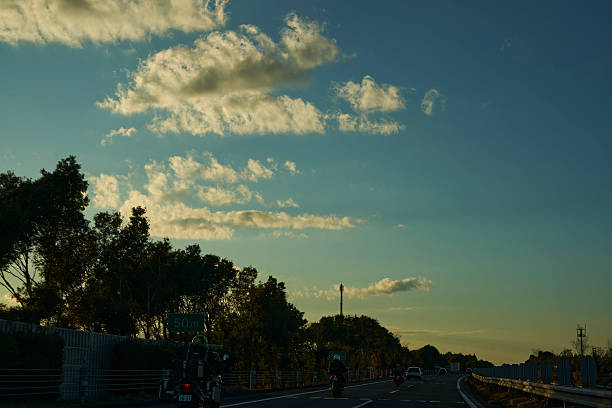 The sinking sun casts streaks of light through clouds, gently enveloping cars on the highway. A moment where the day's end meets the excitement of returning to a place of rest.