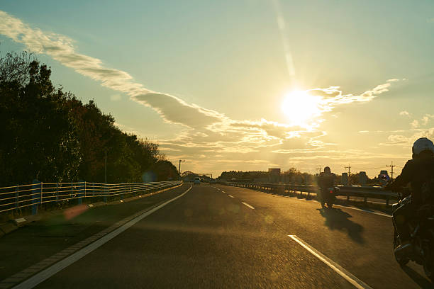 The sinking sun casts streaks of light through clouds, gently enveloping cars on the highway. A moment where the day's end meets the excitement of returning to a place of rest.