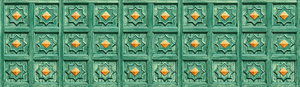 Green wooden panel with relief carving and repeated orange studs creating a traditional pattern