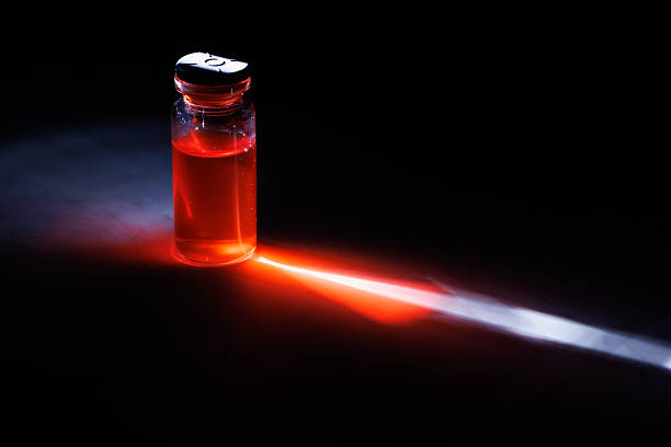 Vibrant glass medical vial with colored liquid reflecting on a marble surface under a sharp light beam against a dark black background for research.