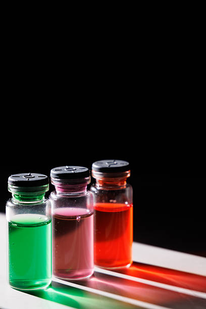 Glass medical bottles with colored liquids casting bright reflections on a marble surface under a beam of light against a dark black background shot.