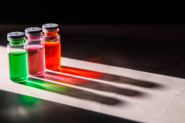 Vibrant glass medical vials with colorful liquids illuminated by a light beam reflecting on a marble surface against a dark black background today.