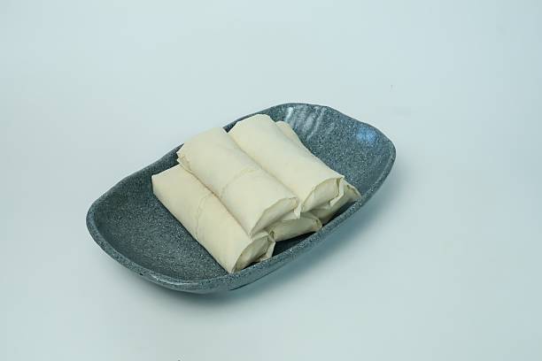 Uncooked Indonesian risoles wrapped in thin pastry, neatly arranged on a ceramic plate and isolated on a white background. Traditional savory snack commonly prepared before frying, photographed in a clean studio style with copy space, suitable for food preparation and frozen food concepts