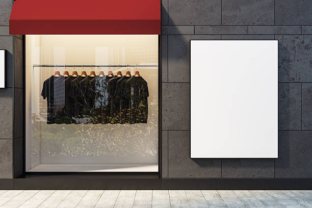 istock Blank vertical poster mockup on modern shopfront wall beside clothing display in storefront window with red canopy on city street facade. 3D Rendering 2253771114