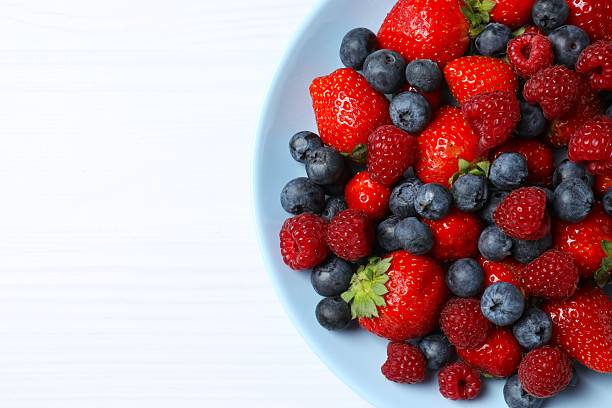 istock Different fresh ripe berries in bowl on wooden table, top view 2253772465