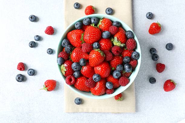 istock Different fresh ripe berries in bowl on wooden table, top view 2253772498