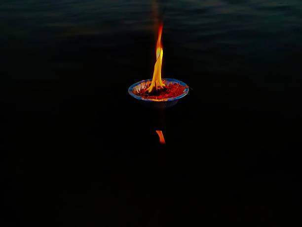 Stock photo showing elevated view of lit diya (oil lamp), with flickering flame in the dark, part of Diwali festival of lights celebration.