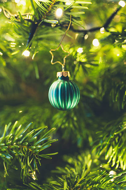 istock Green Christmas bauble hanging on decorated Christmas tree with warm lights 2253775490