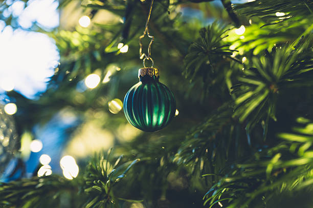 istock Green Christmas ornament hanging on illuminated evergreen tree with soft bokeh 2253777969
