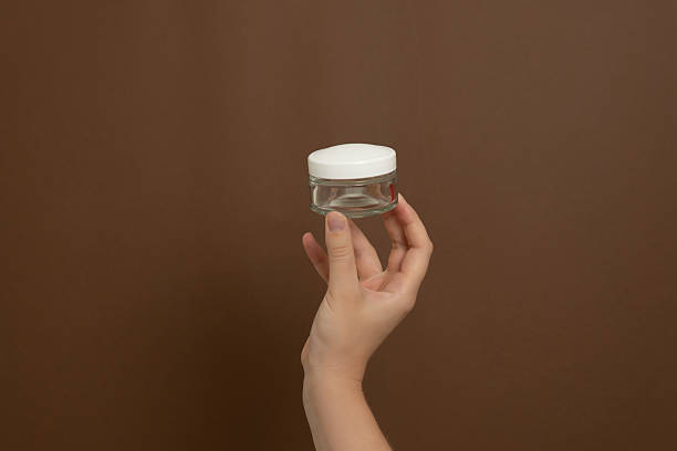 istock Hand holding empty glass skincare jar with white lid 2253778398