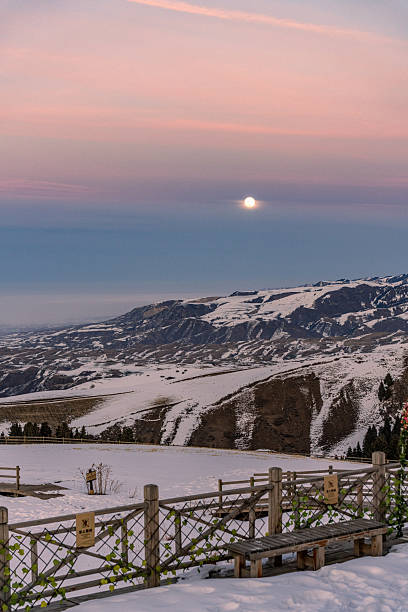 The snow capped mountains and the moon on the evening glow