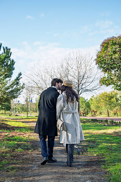 Couple sharing a kiss as they walk together on a path in a natural park during daytime