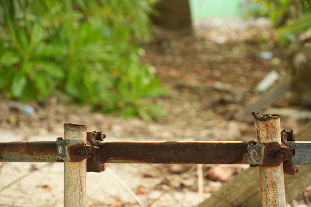 Close-up view of a heavily corroded metal bar, part of an old fence, with lush green tropical foliage in the soft-focus background.