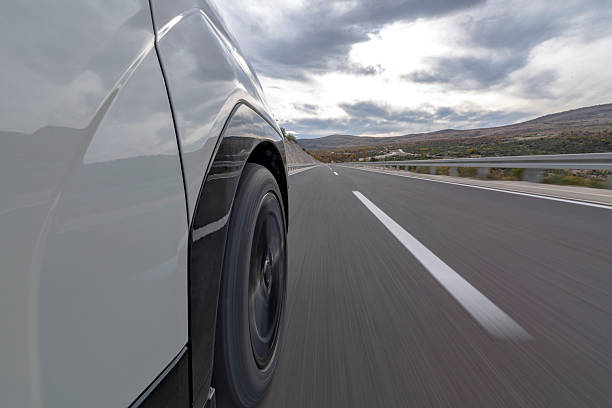 Blurred action from a car at high speed, showing a spinning wheel and a metal fence next to the road