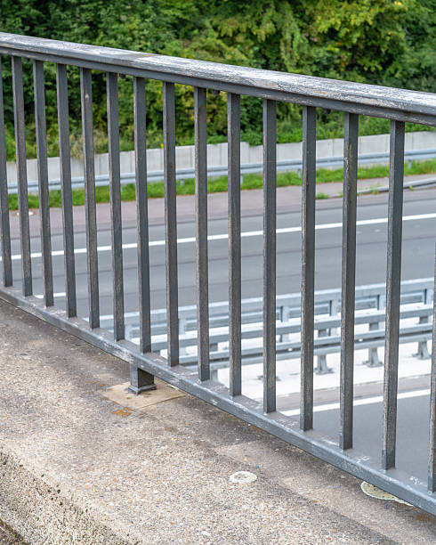 istock Metal railing along a bridge overlooking a busy highway surrounded by green trees on a clear day 2253787012