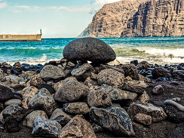 Pebbles on a volcanic beach by the ocean and cliffs in los gigantes, tenerife