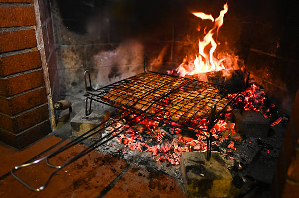 Grilling meat on a wire rack over glowing embers and burning wood in a brick fireplace