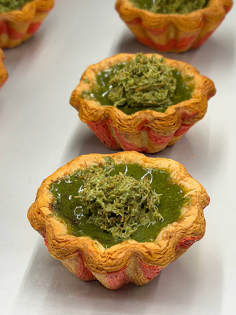 Image of bakery display of rows of freshly baked pastries on tray, Dubai pistachio chocolate flavoured Portuguese custard tarts (pastéis de nata), floral shaped laminated flaky pastry cases filled with egg custard, kadaif garnish, focus on foreground