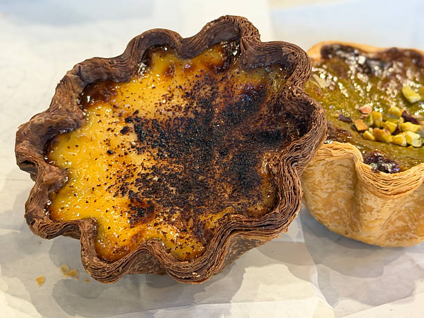 Close-up image of two of freshly baked  pastries on plate, Dubai pistachio chocolate flavoured and traditional Portuguese custard tarts (pastéis de nata), floral shaped laminated flaky pastry cases filled with egg custard, focus on foreground