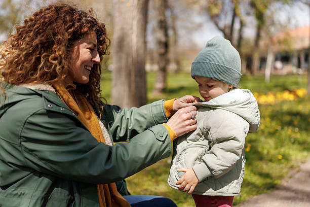 istock Caring mother buttoning her daughter's jacket during cold early spring day in the park 2253797727
