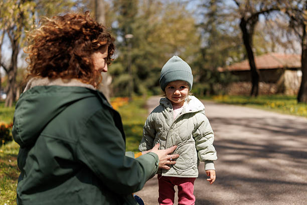 istock Caring mother buttoning her daughter's jacket during cold early spring day in the park 2253797738