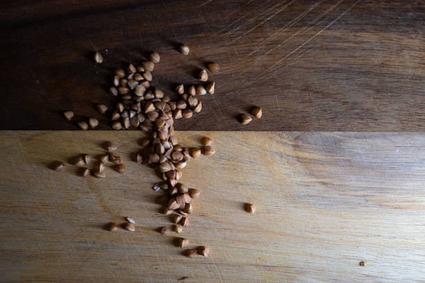 Gentle lighting casts shadows that reveal textured nature of spilled buckwheat and crumbs on surface of wood