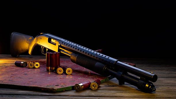 istock Black pump-action shotgun with red shells on a rustic wooden table under dramatic lighting. 2253799979