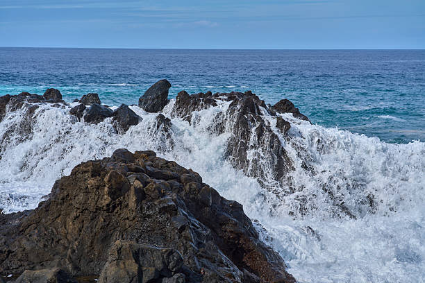 Atlantic Ocean waves crashing against volcanic rocks at El Bollullo beach with dramatic white spray and foam in Tenerife Canary Islands