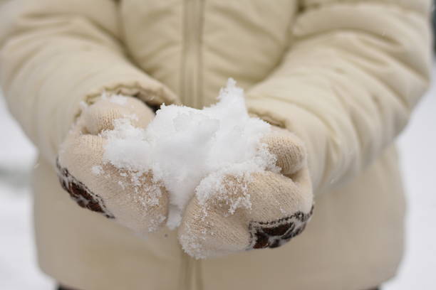 Girl in a light jacket and knitted mittens holding snow in her hands. Winter, fresh snow, feeling of cold and warmth.
