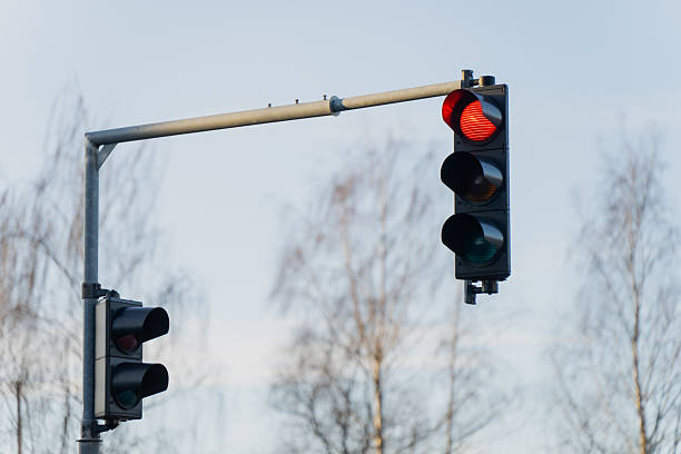 istock Red traffic light signal illuminated on urban intersection pole with pedestrian signal and metal support arm against pale winter sky and bare trees 2253806569