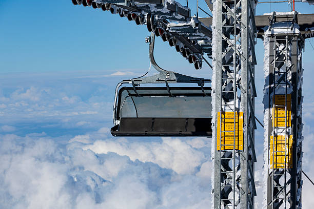 Empty chairlift suspended above a cloud layer in a snowy alpine mountain landscape. Winter conditions, high altitude and cable car infrastructure symbolize mountain tourism, skiing and alpine transport.