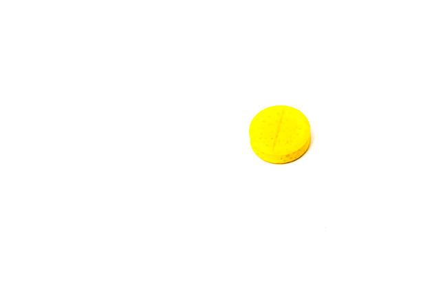 A close-up, isolated shot of a single, small yellow pill with a scored line on top, on a clean white background.