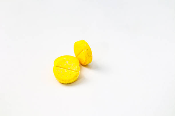 Two bright yellow pills are isolated on a clean white background, with one in sharp focus.