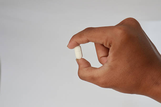 istock Human Hand Holding Small White Pill Between Fingers Studio Lighting Against White Background 2253808312