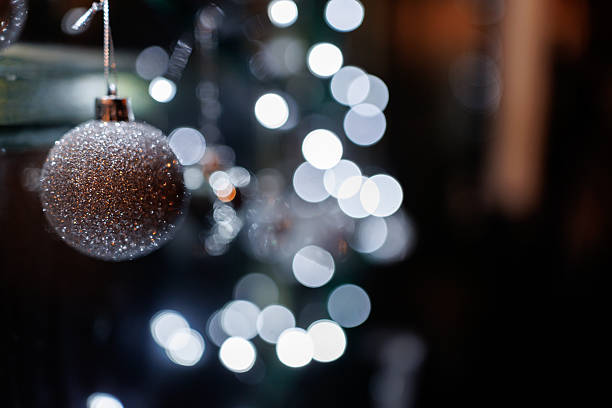 Silver colored ornaments and Christmas lights on window shining in night