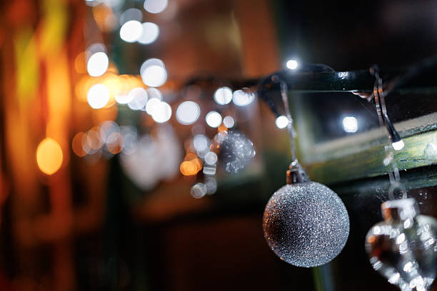 Silver colored ornaments and Christmas lights on window shining in night