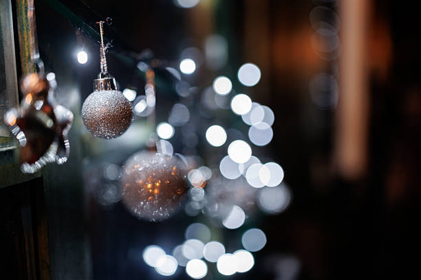 Silver colored ornaments and Christmas lights on window shining in night