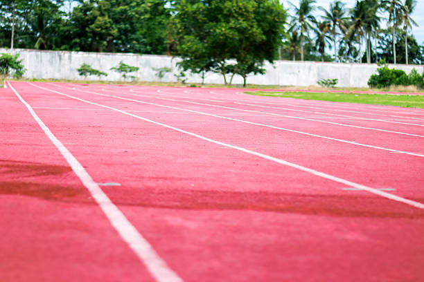 Close-up view of an empty red running track with white lane markers, set against a backdrop of green grass and trees.