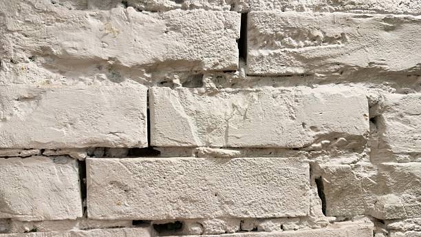 istock Close-up of a white painted brick wall with cracks, texture, and uneven surface for design 2253818636