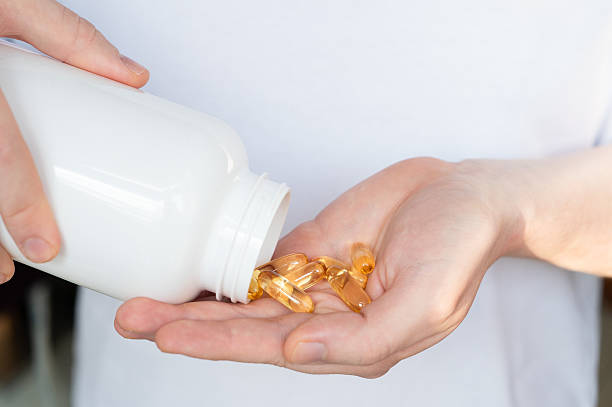 istock Hand pouring fish oil capsules from a white bottle into palm. 2253827549