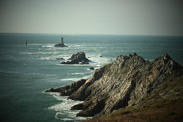 A cap with some rocks and a lighthouse with lots of waves around.