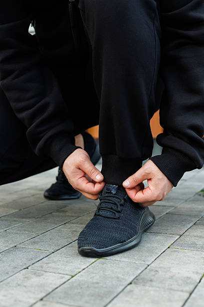 istock An athlete is expertly tying their shoelaces and preparing for an intense workout while wearing stylish black sportswear, positioned on a firm pavement surface to maximize performance 2253829863